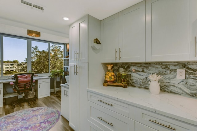 interior space with backsplash, light stone countertops, light hardwood / wood-style flooring, and white cabinets