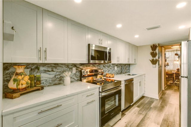 kitchen featuring light stone countertops, light hardwood / wood-style flooring, decorative backsplash, white cabinets, and appliances with stainless steel finishes