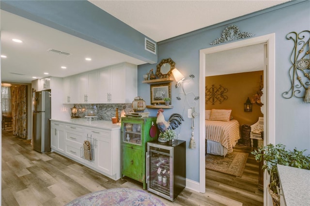 kitchen with light wood-type flooring, white cabinetry, stainless steel refrigerator, and tasteful backsplash