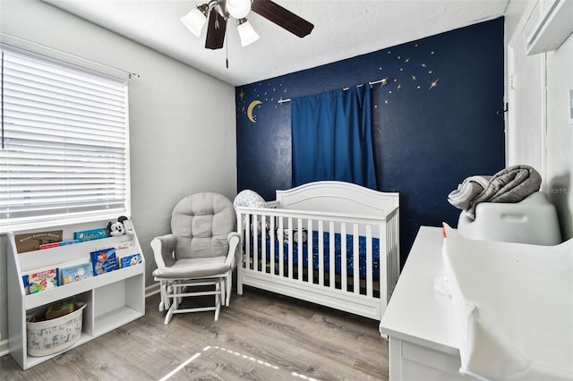 bedroom with ceiling fan, wood-type flooring, and a crib