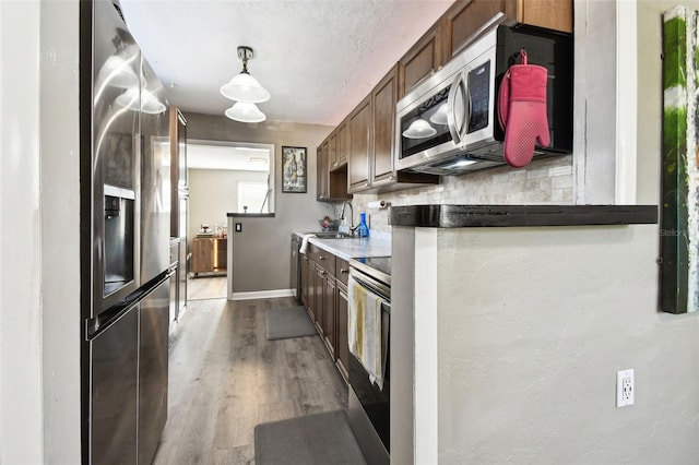 kitchen featuring decorative backsplash, appliances with stainless steel finishes, light wood-type flooring, and pendant lighting