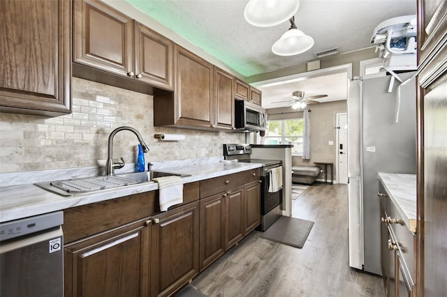 kitchen with dark brown cabinetry, ceiling fan, hanging light fixtures, stainless steel appliances, and light hardwood / wood-style flooring