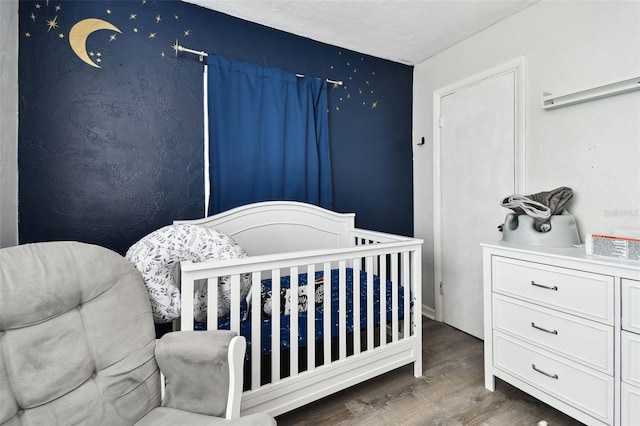 bedroom with a textured ceiling, a nursery area, and dark hardwood / wood-style floors