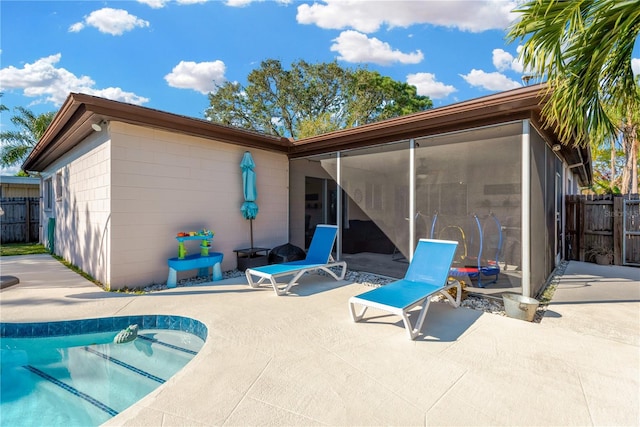 rear view of house featuring a sunroom, a patio area, and a fenced in pool