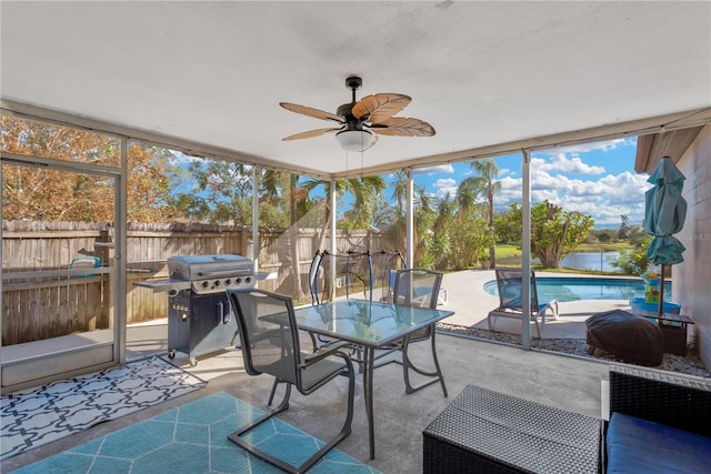 sunroom with ceiling fan and a water view