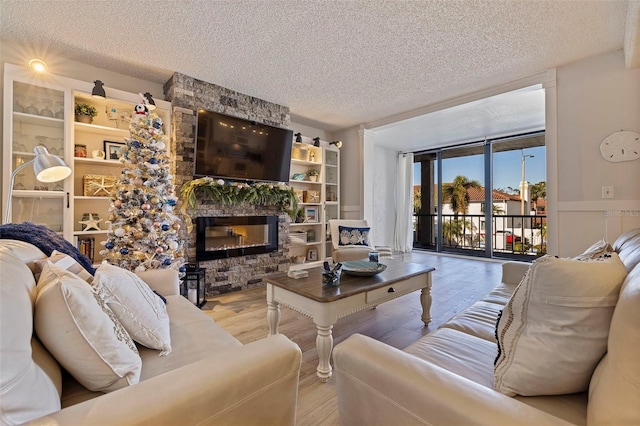 living room featuring expansive windows, a stone fireplace, light wood-type flooring, and a textured ceiling