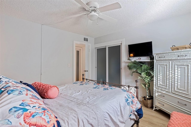 bedroom with a textured ceiling, a closet, light hardwood / wood-style flooring, and ceiling fan