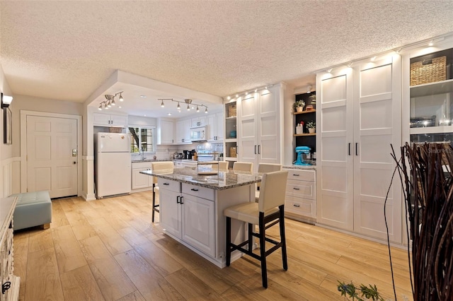 kitchen featuring a breakfast bar, light wood-style flooring, white appliances, white cabinetry, and open shelves