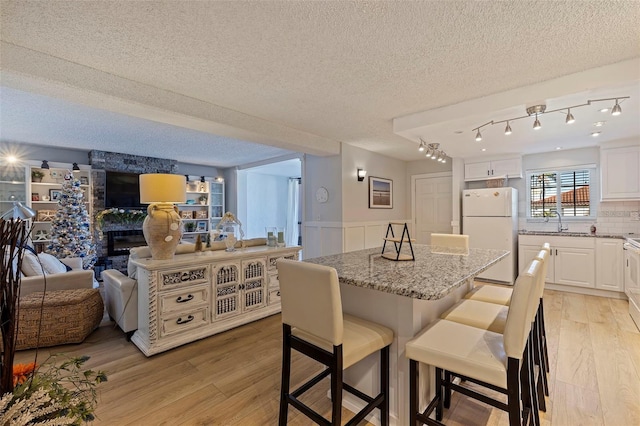 dining space featuring a textured ceiling, light wood-style flooring, and wainscoting