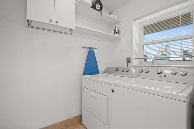 clothes washing area featuring cabinets, light tile patterned flooring, and washing machine and dryer