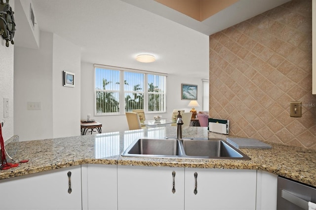 kitchen featuring tasteful backsplash, dishwasher, sink, white cabinets, and light stone counters