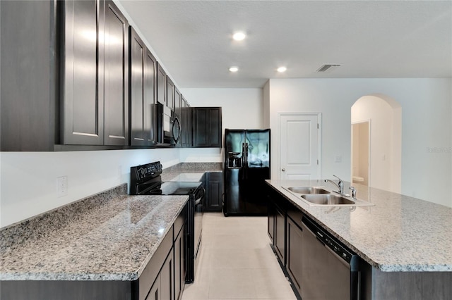 kitchen featuring light stone countertops, sink, a center island with sink, and black appliances