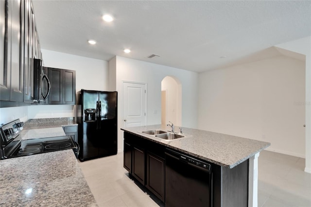 kitchen with light stone countertops, a center island with sink, black appliances, and sink