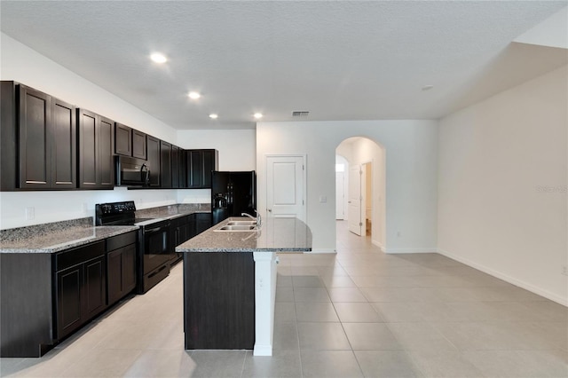 kitchen featuring light stone countertops, a textured ceiling, black appliances, light tile patterned floors, and an island with sink