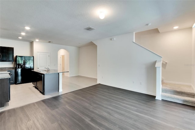 kitchen featuring a kitchen island with sink, sink, light hardwood / wood-style floors, and black refrigerator with ice dispenser