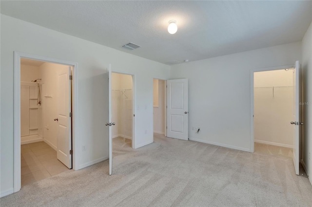 unfurnished bedroom with a closet, light colored carpet, a spacious closet, and ensuite bath