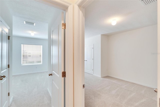 hallway with a textured ceiling and light carpet