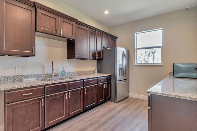 kitchen with stainless steel refrigerator with ice dispenser, light stone counters, dark brown cabinetry, sink, and light hardwood / wood-style flooring