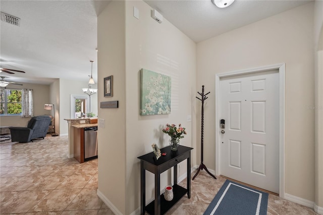 foyer with ceiling fan with notable chandelier, light tile patterned floors, and a textured ceiling