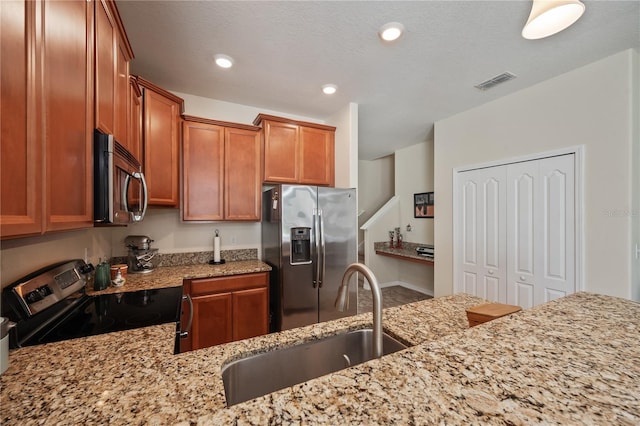 kitchen featuring light stone counters, sink, stainless steel appliances, and a textured ceiling