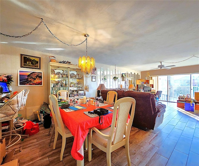 dining space with ceiling fan with notable chandelier and hardwood / wood-style flooring