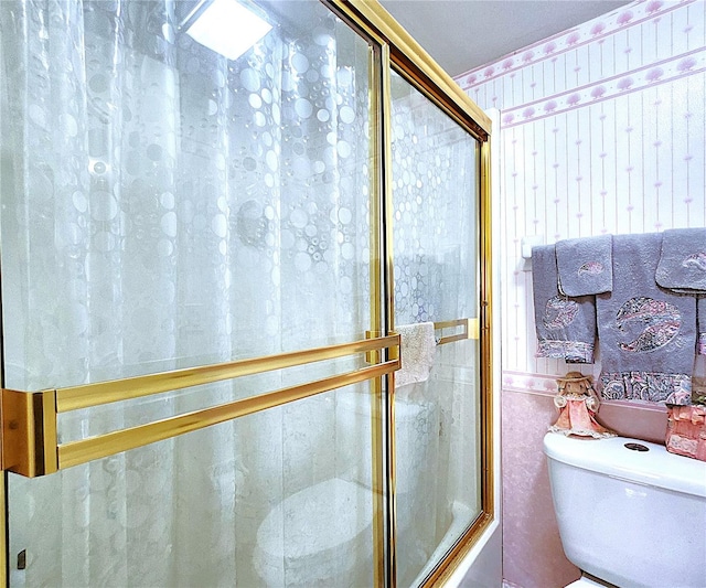 bathroom with combined bath / shower with glass door and toilet