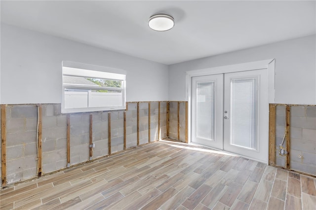 unfurnished room with french doors, tile walls, and light wood-type flooring