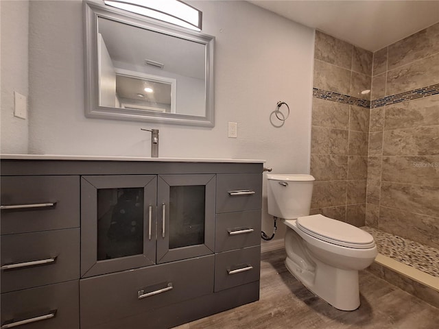 bathroom featuring vanity, toilet, wood-type flooring, and tiled shower