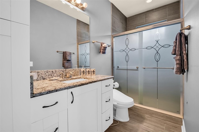 bathroom featuring toilet, vanity, a shower with shower door, and hardwood / wood-style flooring