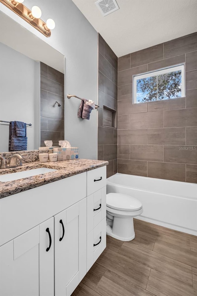 full bathroom with vanity, hardwood / wood-style flooring, toilet, and tiled shower / bath