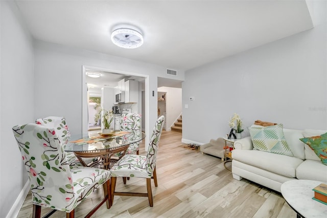 dining room with stairway, light wood-type flooring, visible vents, and baseboards