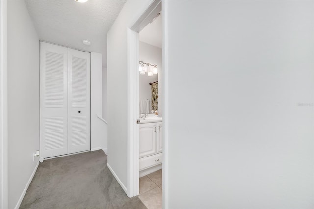 hallway featuring a sink, a textured ceiling, baseboards, and carpet flooring