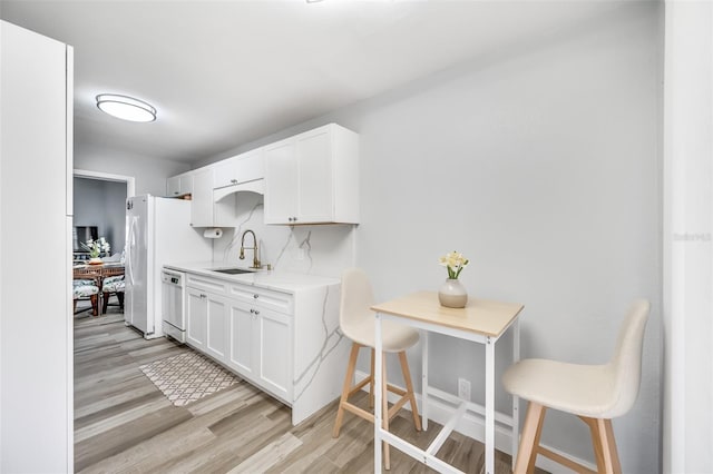 kitchen with light wood-style floors, white cabinets, a sink, light stone countertops, and dishwasher