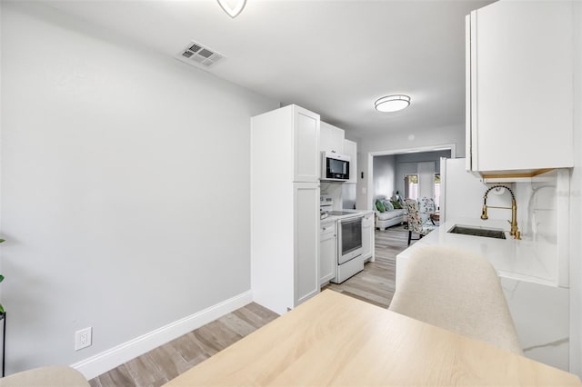 kitchen with white electric range oven, light wood finished floors, visible vents, white cabinetry, and a sink