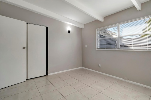 unfurnished bedroom featuring beamed ceiling, light tile patterned floors, and a closet