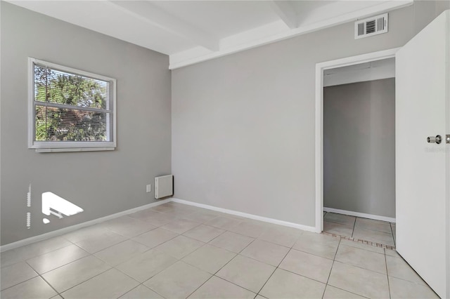 tiled empty room featuring beam ceiling