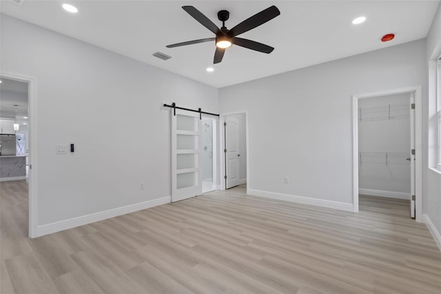 unfurnished bedroom with light hardwood / wood-style flooring, ceiling fan, a barn door, a spacious closet, and a closet