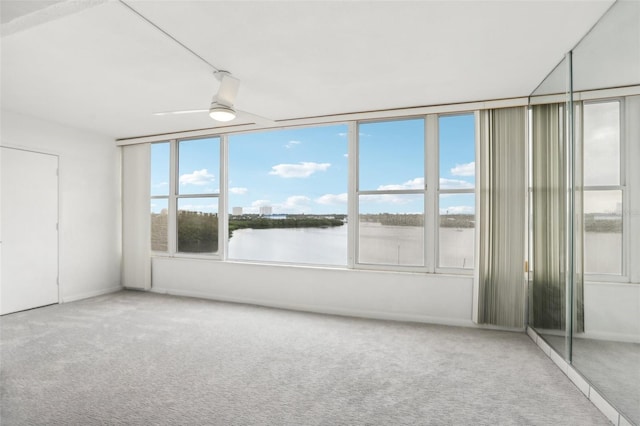 carpeted spare room with a water view and ceiling fan