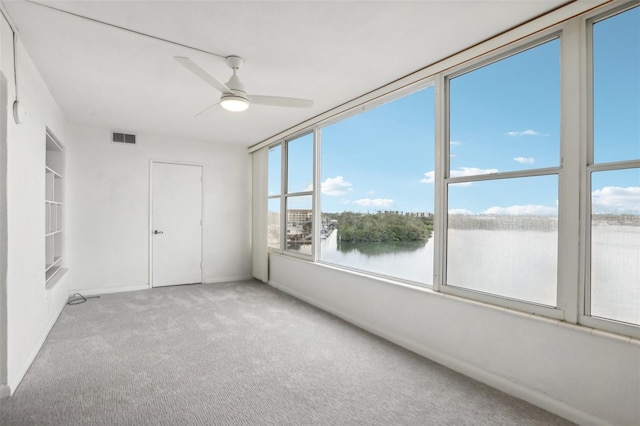 interior space featuring carpet, ceiling fan, a healthy amount of sunlight, and a water view