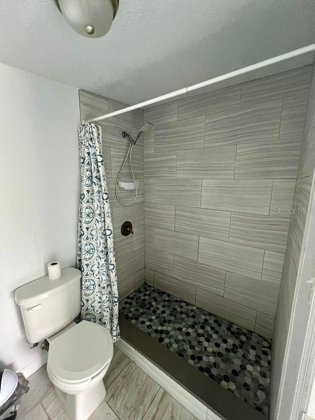 bathroom featuring a shower with curtain, toilet, and a textured ceiling