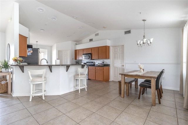 kitchen with an inviting chandelier, vaulted ceiling, appliances with stainless steel finishes, a kitchen bar, and kitchen peninsula