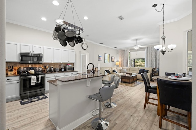 kitchen with backsplash, a kitchen island with sink, pendant lighting, white cabinetry, and black / electric stove