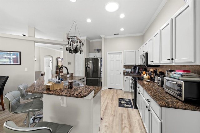 kitchen featuring appliances with stainless steel finishes, dark stone counters, sink, white cabinetry, and an island with sink