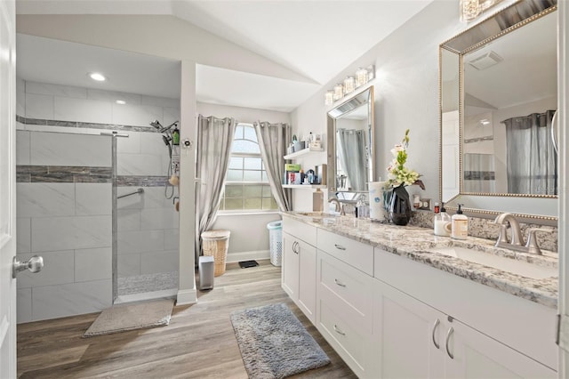 bathroom with a tile shower, vanity, hardwood / wood-style flooring, and vaulted ceiling