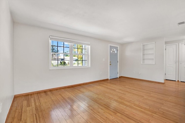 spare room with built in shelves and light hardwood / wood-style floors