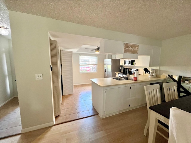 kitchen with white cabinets, kitchen peninsula, stainless steel appliances, and light hardwood / wood-style flooring