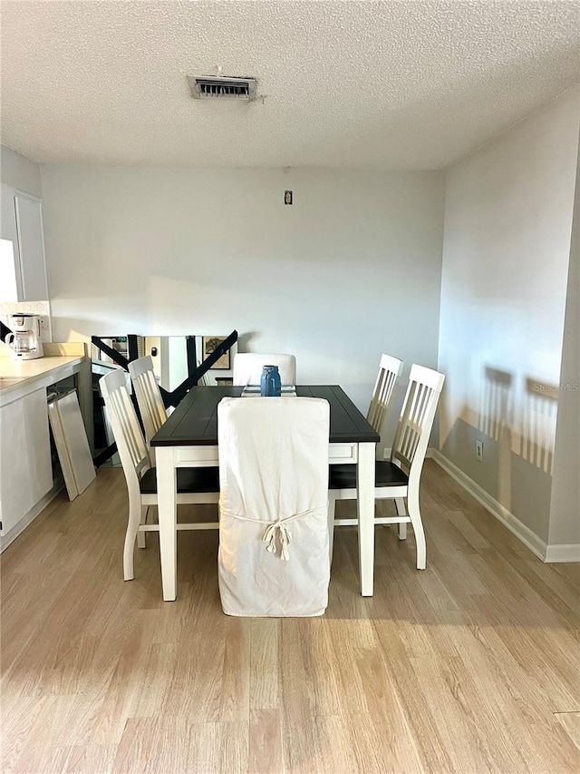 dining area with a textured ceiling and light hardwood / wood-style flooring