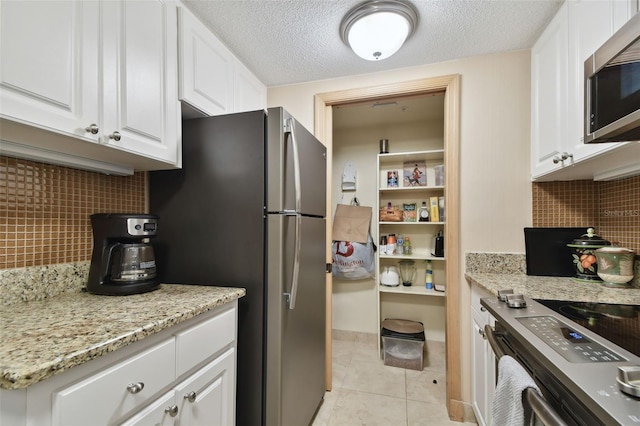 kitchen featuring tasteful backsplash, a textured ceiling, stainless steel appliances, light tile patterned floors, and white cabinets