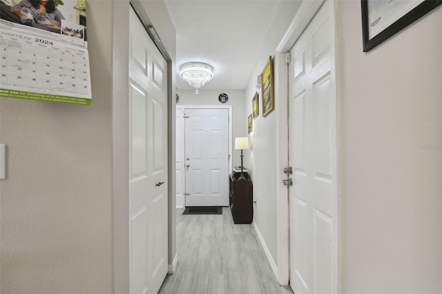 corridor featuring an inviting chandelier, baseboards, and light wood finished floors