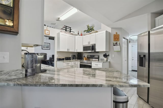 kitchen with vaulted ceiling, light stone counters, a peninsula, white cabinets, and stainless steel appliances